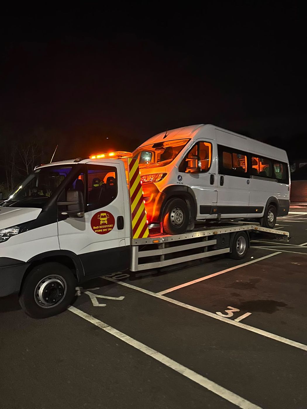 Minibus recovered onto a BnD Recovery flatbed truck at night with amber beacons lit