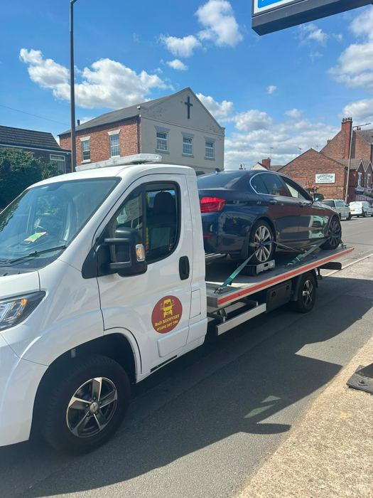Dark blue BMW saloon on a BnD Recovery flatbed truck on a village high street
