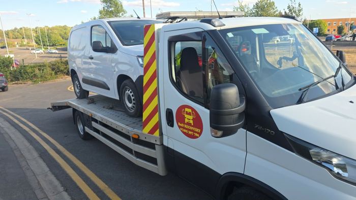 Small white van on a BnD Recovery flatbed truck in a retail park
